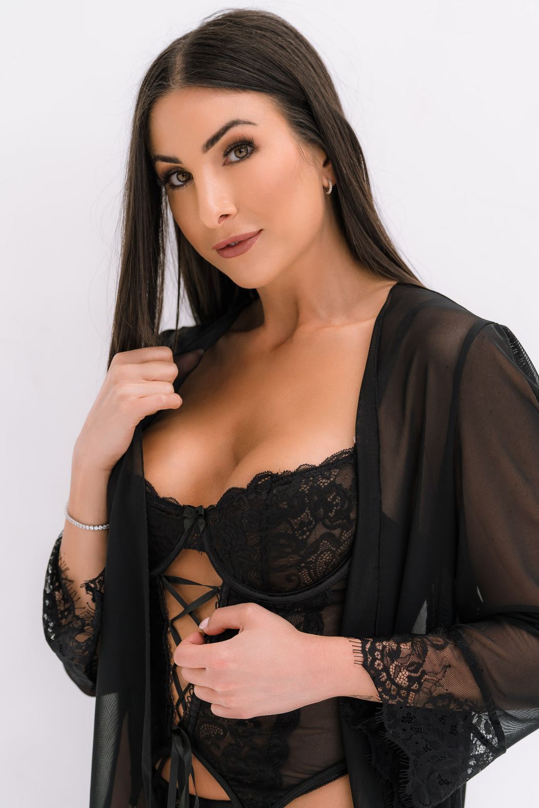 Woman in black lace lingerie and a sheer robe, hands at the collar