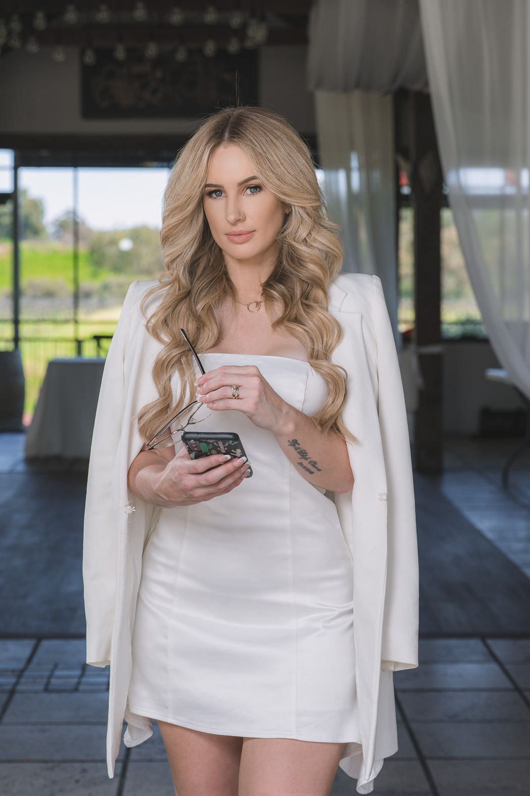 Woman in a white dress holding her phone in a glass pavilion