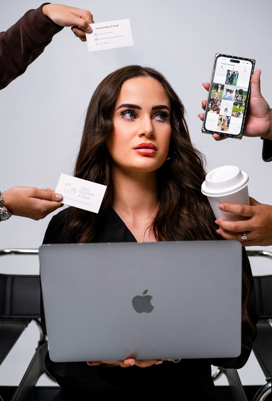 Woman at a laptop surrounded by hands holding business cards, a phone and coffee