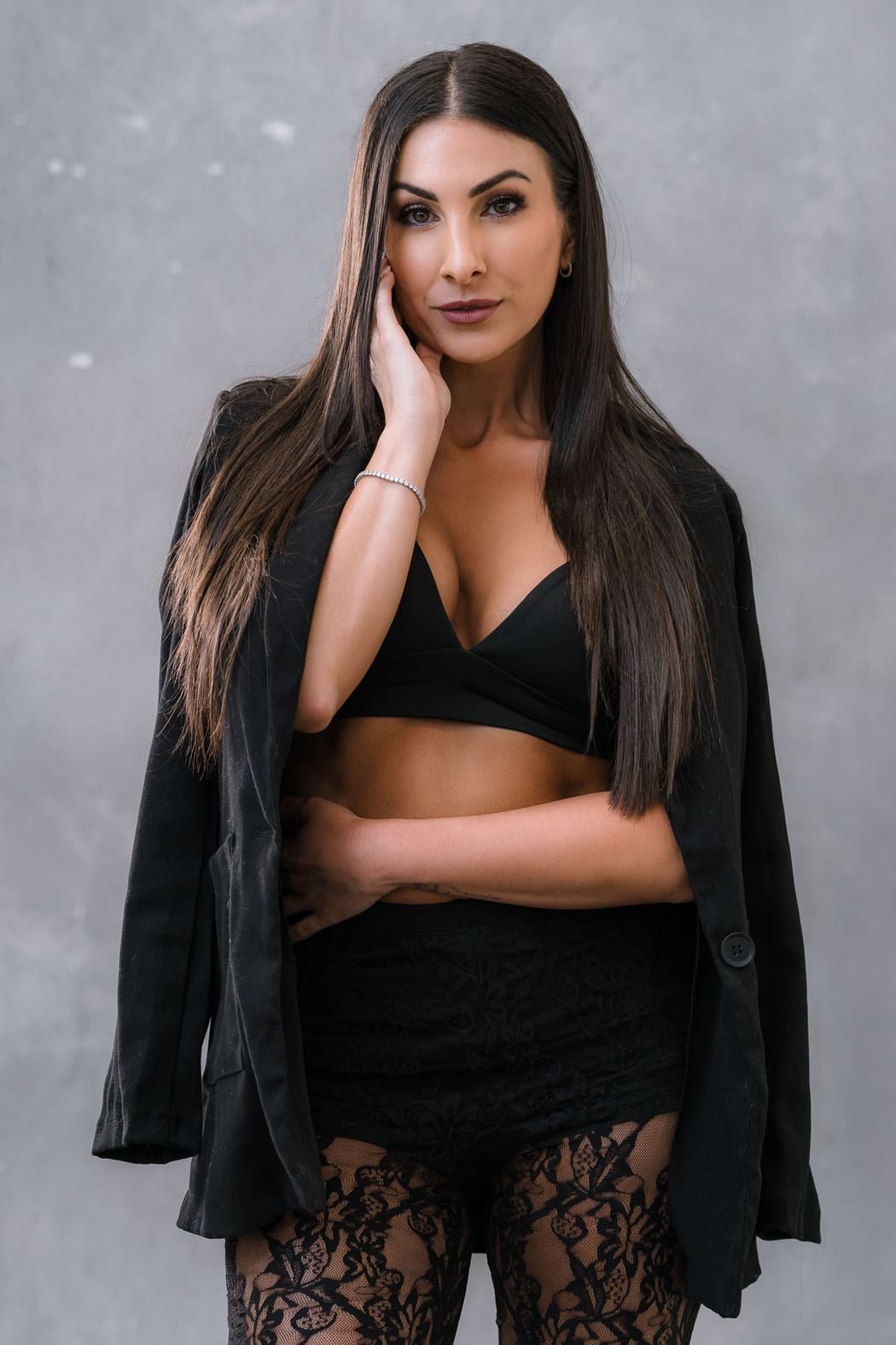 Woman in a black blazer and lace trousers, hand to her face