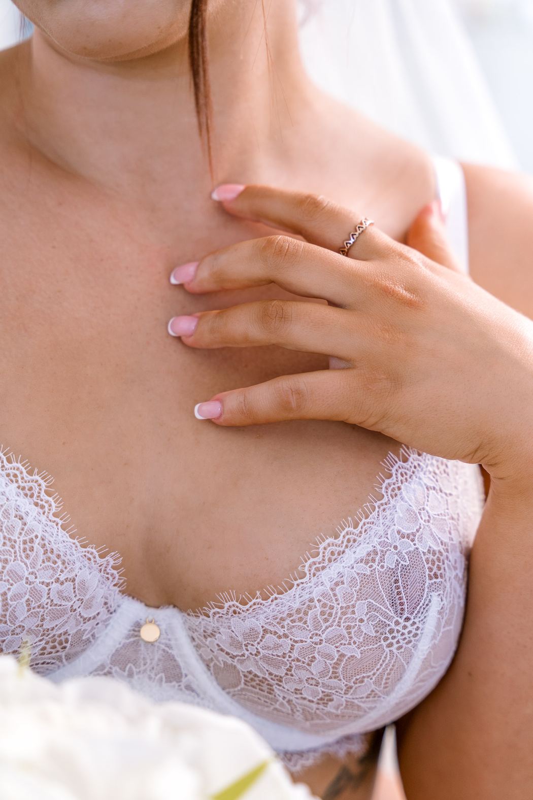 Detail of a white lace bra and a hand on the collarbone