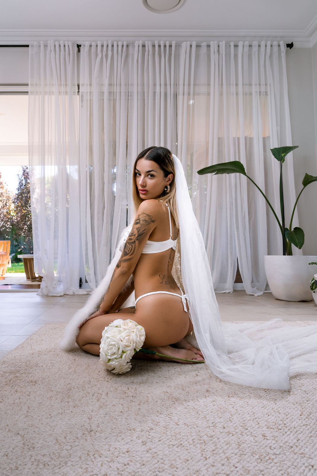 Bride kneeling on the rug in a long veil, looking over her shoulder