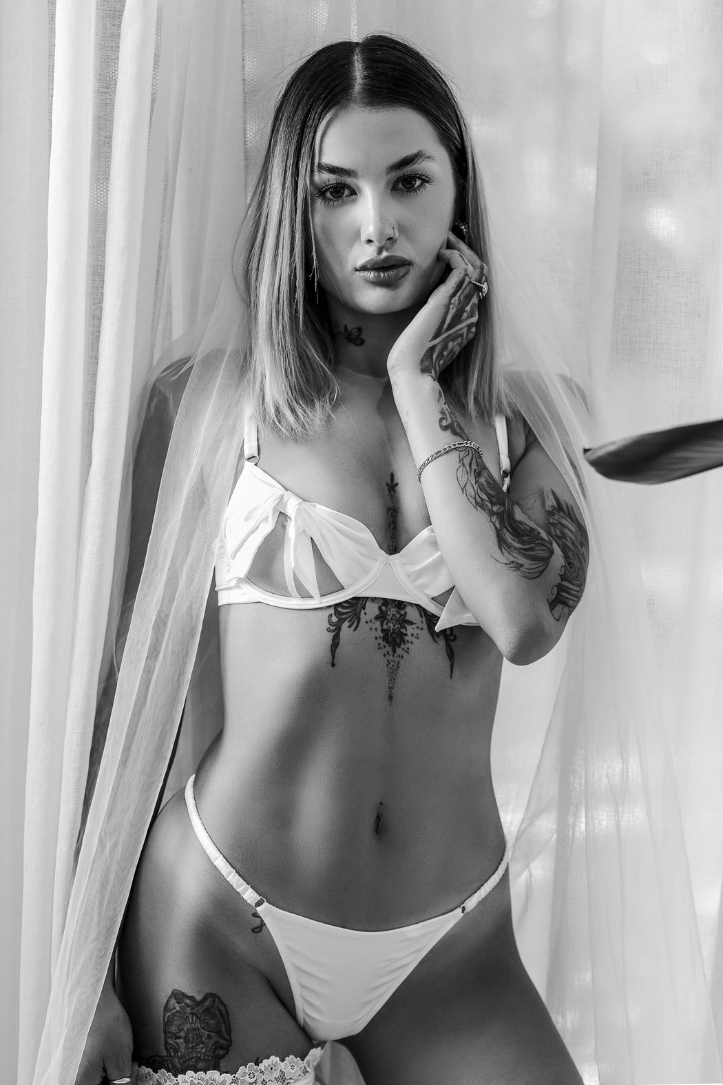 Black and white bridal portrait, hand to face by the curtains