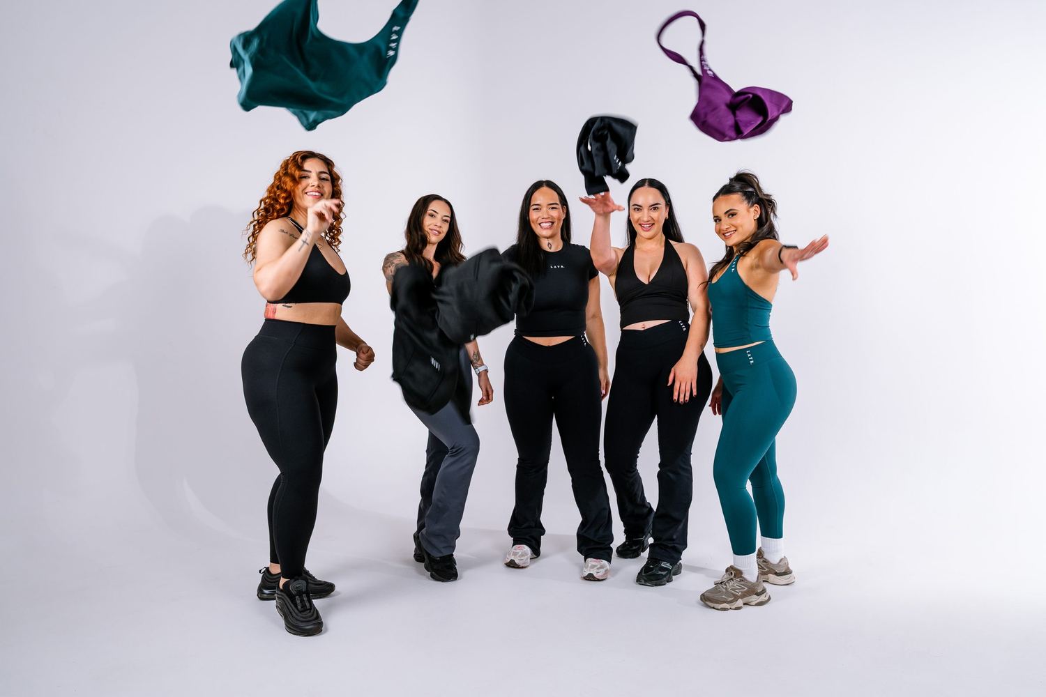 Five women in activewear tossing clothes in the air