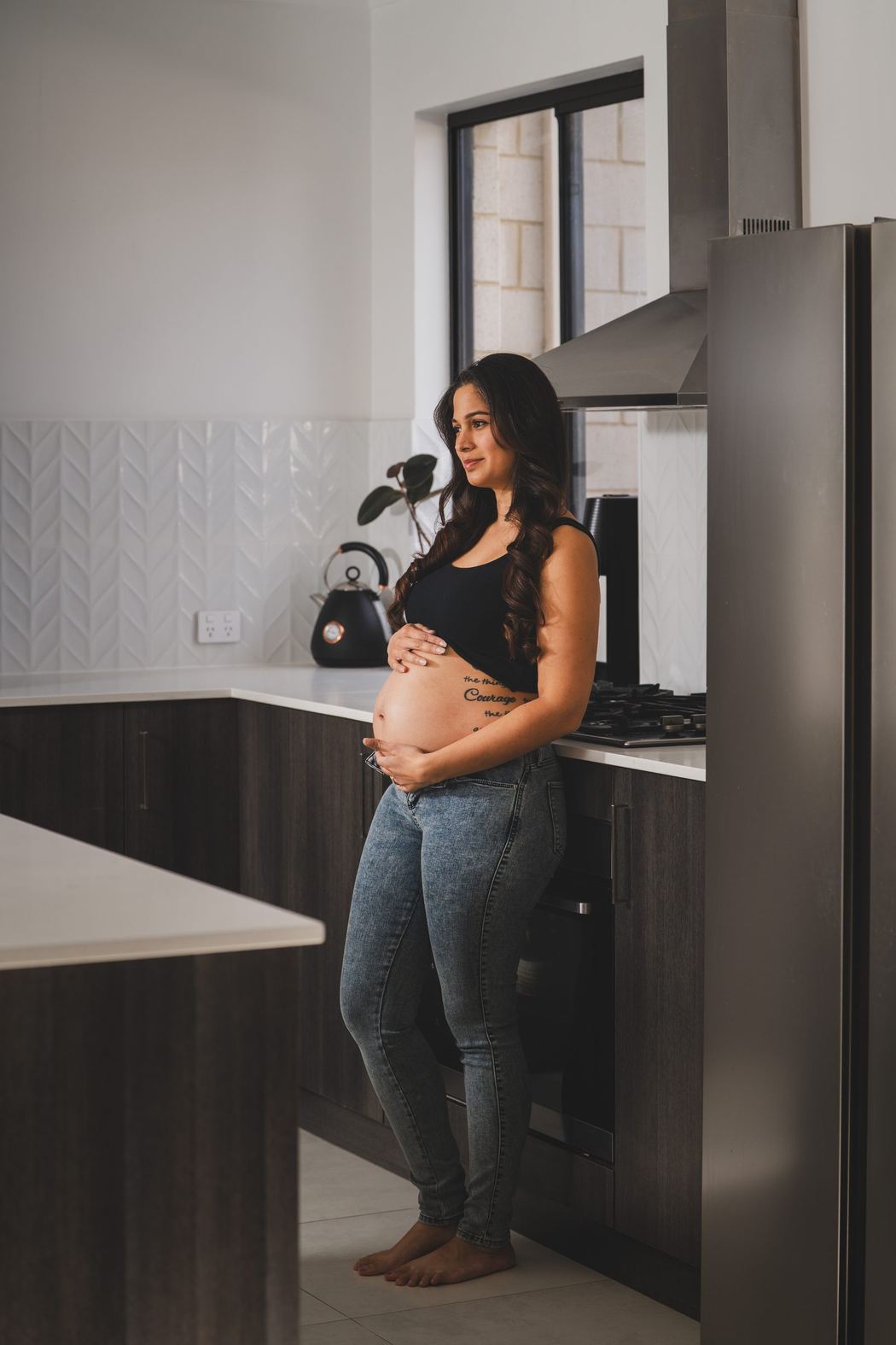 Expecting mother standing in her kitchen, hands on her belly
