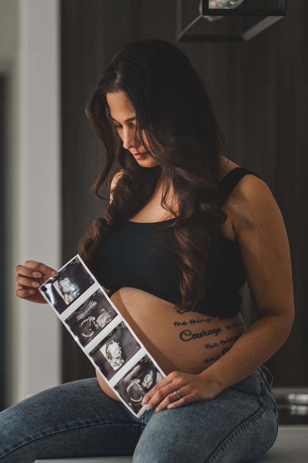 Expecting mother seated, looking down at ultrasound photos