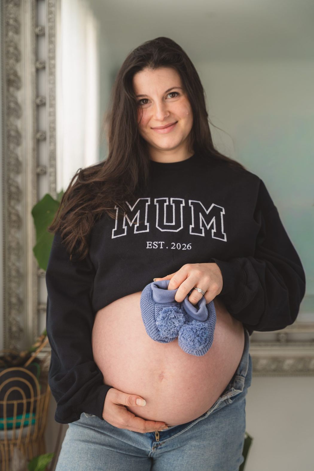 Smiling expecting mother in a Mum sweatshirt holding baby booties